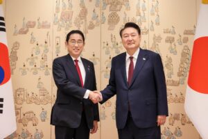 Japanese Prime Minister Fumio Kishida shaking hands with South Korean President Yoon Suk-yeol, with their flags behind them.